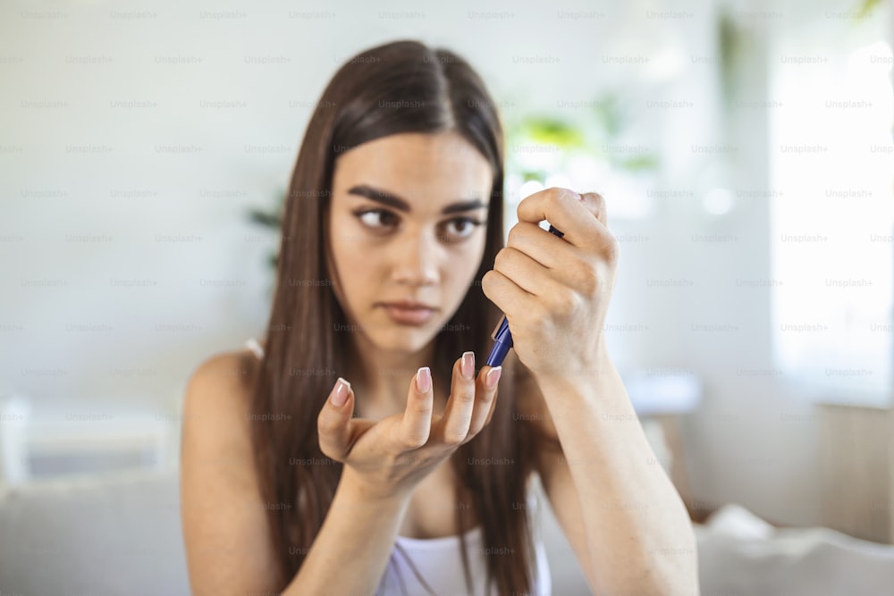 指にランスレットを使う女性。自宅のリビングで血糖値検査をしている女性。