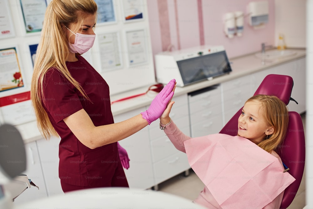 Gives high five. Little girl visiting dentist in clinic. Conception of stomatology.