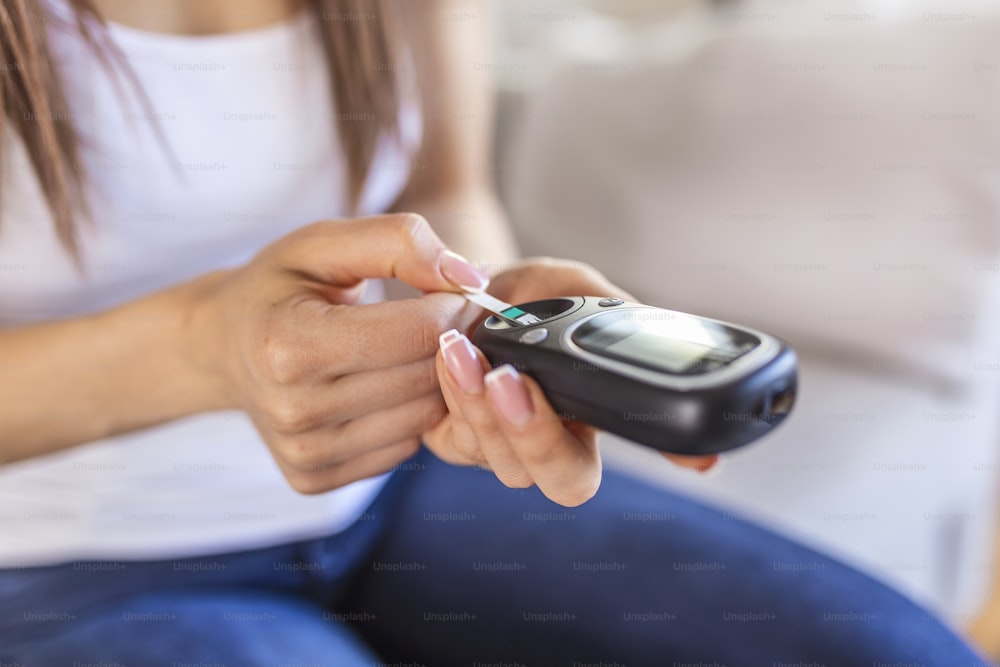 Woman with glucometer checking blood sugar level at home. Diabetes, health care concept. Young woman using digital glucometer at home. Diabetes control