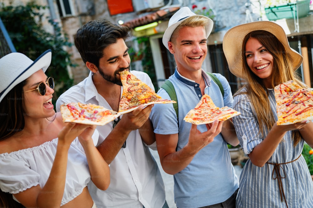 Happy group of people eating pizza outdoors, they are enjoying together.