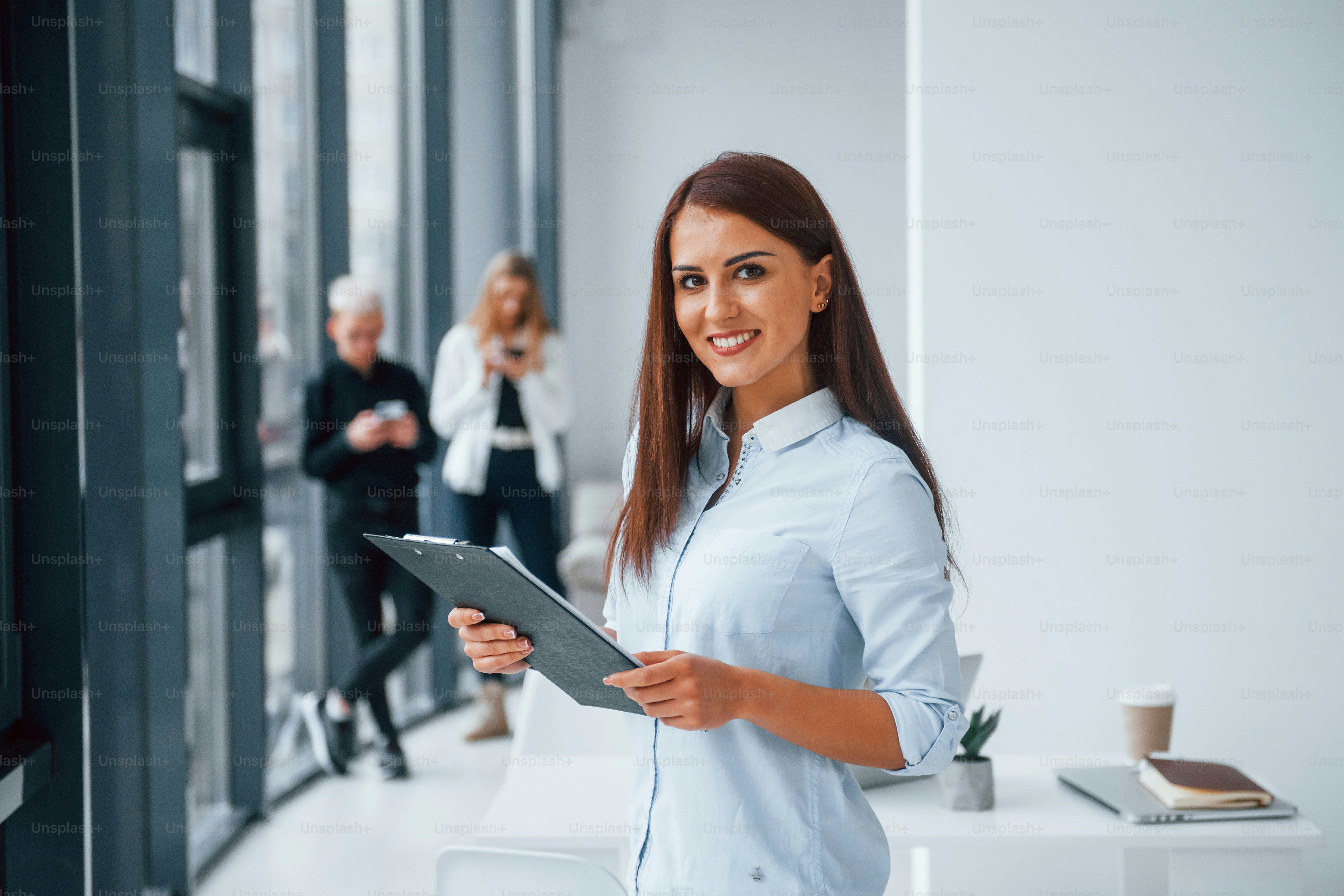 Portrait of woman with notepad that standing in front of group of young successful team that working and communicating together indoors in office.
