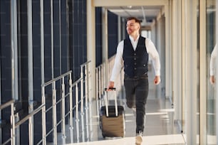 Un pasajero masculino joven con ropa formal elegante está en el vestíbulo del aeropuerto.
