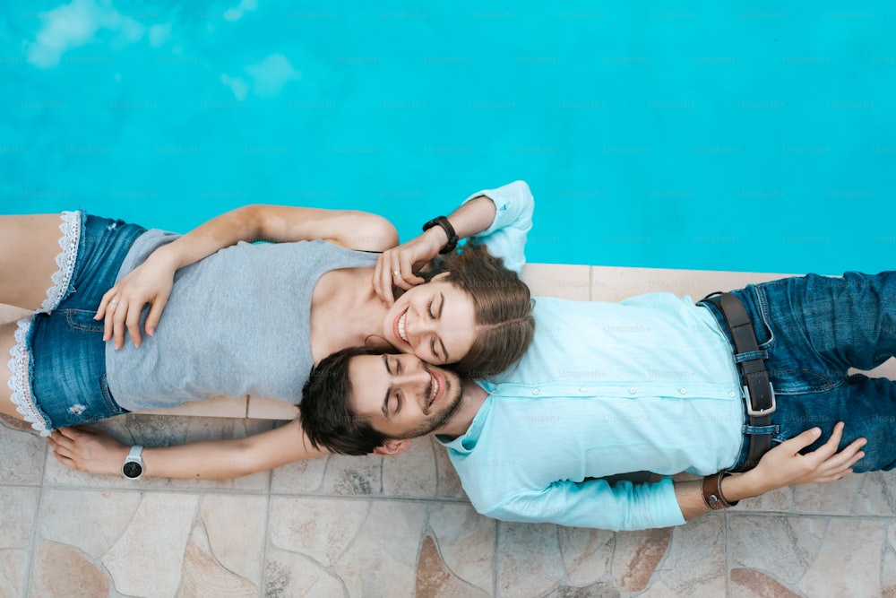 Retrato de casal sorridente deitado vestido perto da piscina. Eles adoram um ao outro
