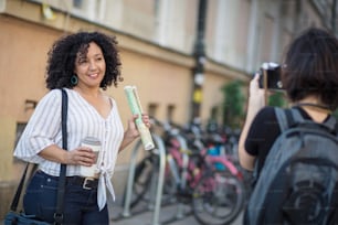 Mulher sorridente em pé na rua com xícara de café. Mulher tirando foto dela.