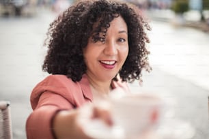 Smiling woman at cafe taking mug of coffee. Focus is on background.