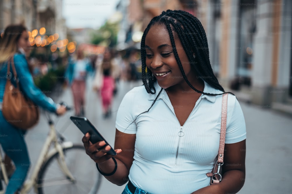 낮 동안 도시에 있는 동안 스마트폰을 사용하는 아름다운 아프리카계 미국인 여성