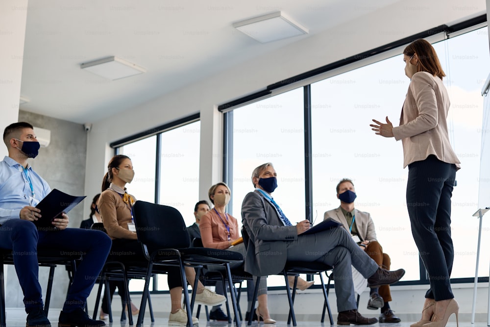 Vista inferior de un líder empresarial con mascarilla comunicándose con un grupo de sus compañeros de trabajo en un seminario en la sala de conferencias.