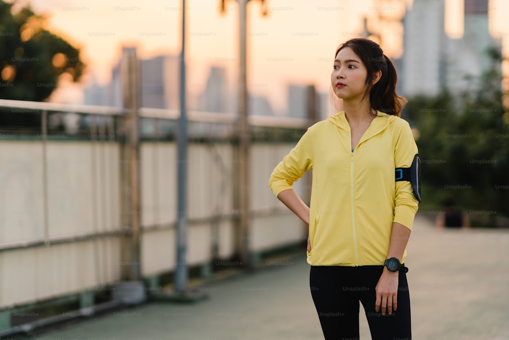 Beautiful young Asia athlete lady exercises doing stretch work out in urban environment. Japanese teen girl wearing sports clothes on walkway bridge in early morning. Lifestyle active sporty in city.