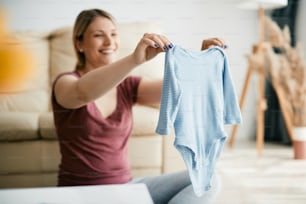 Close-up of mother holding baby bodysuit for boys at home.