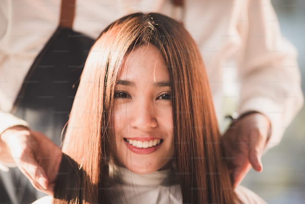 Professional hirdresser design the hair style of smilling young lady with bright brown colour and cutting at salon barber