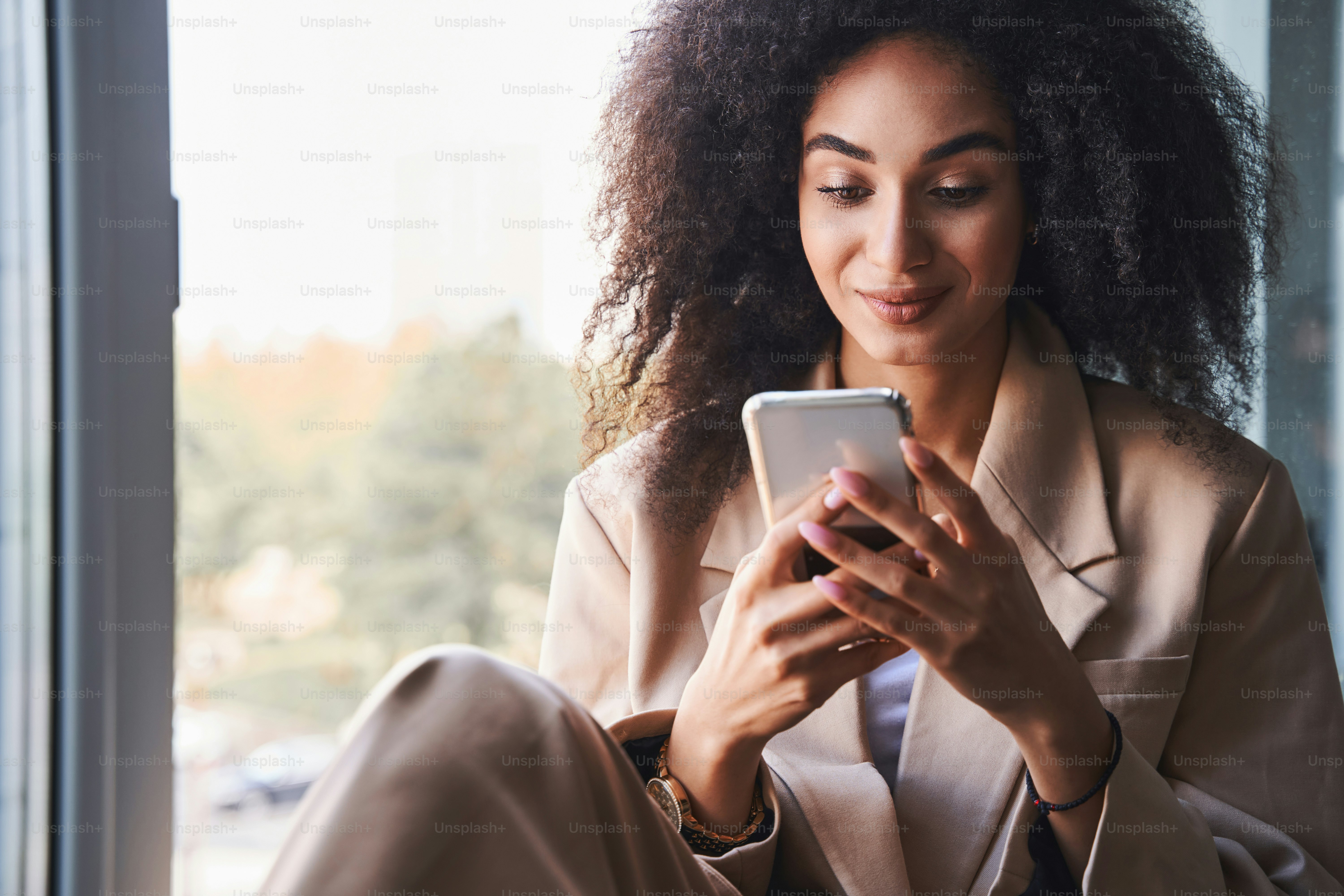 Close up photo of a beautiful long haired lady smiling while looking at the screen of a smartphone
