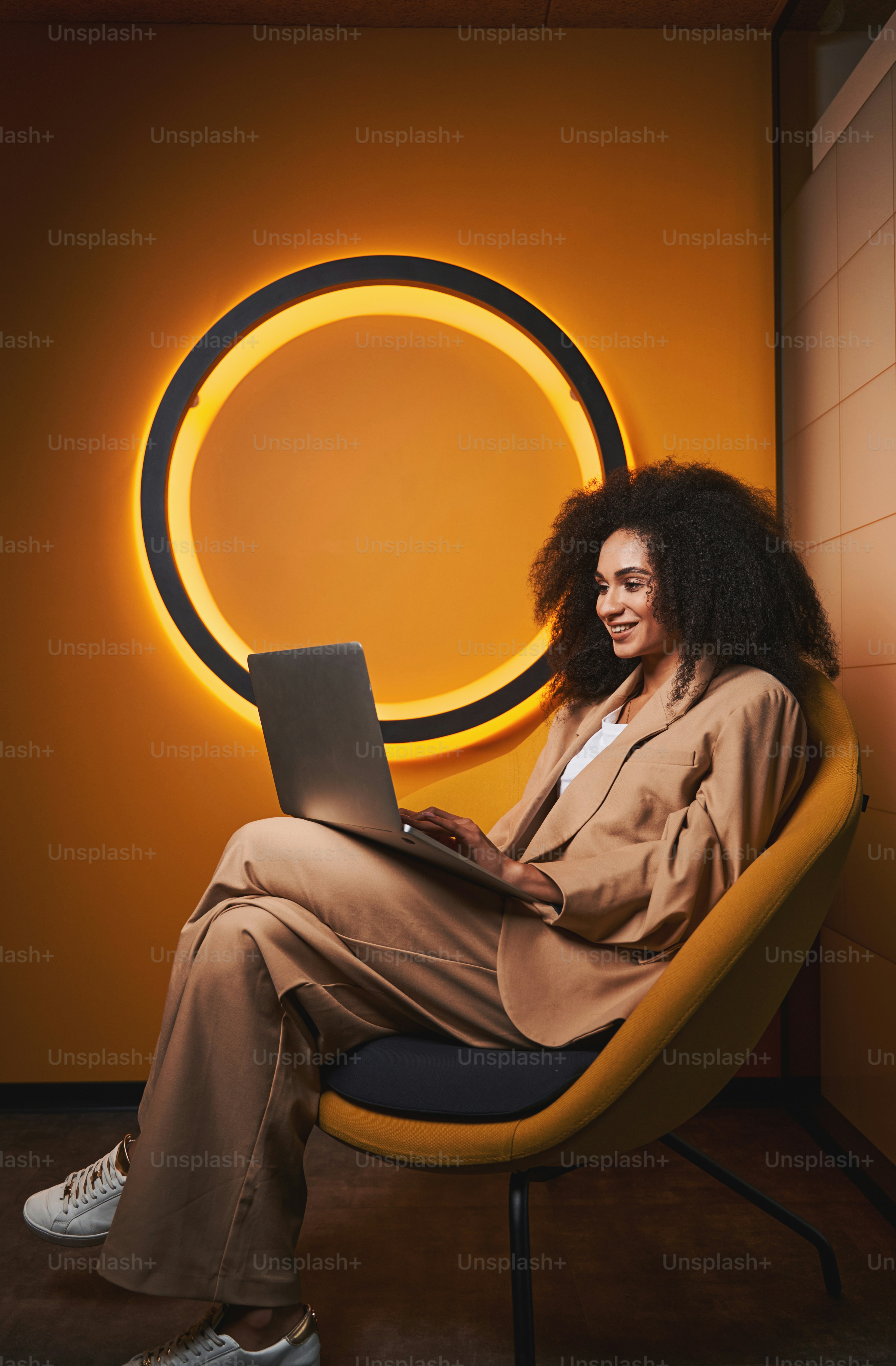 ラップトップを膝の上に置いて肘掛け椅子に座り、オンラインでコミュニケーションをとるかわいい女性