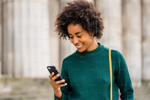 Portrait of afro business woman using her mobile phone while standing outdoors at the street. Business and urban concept.