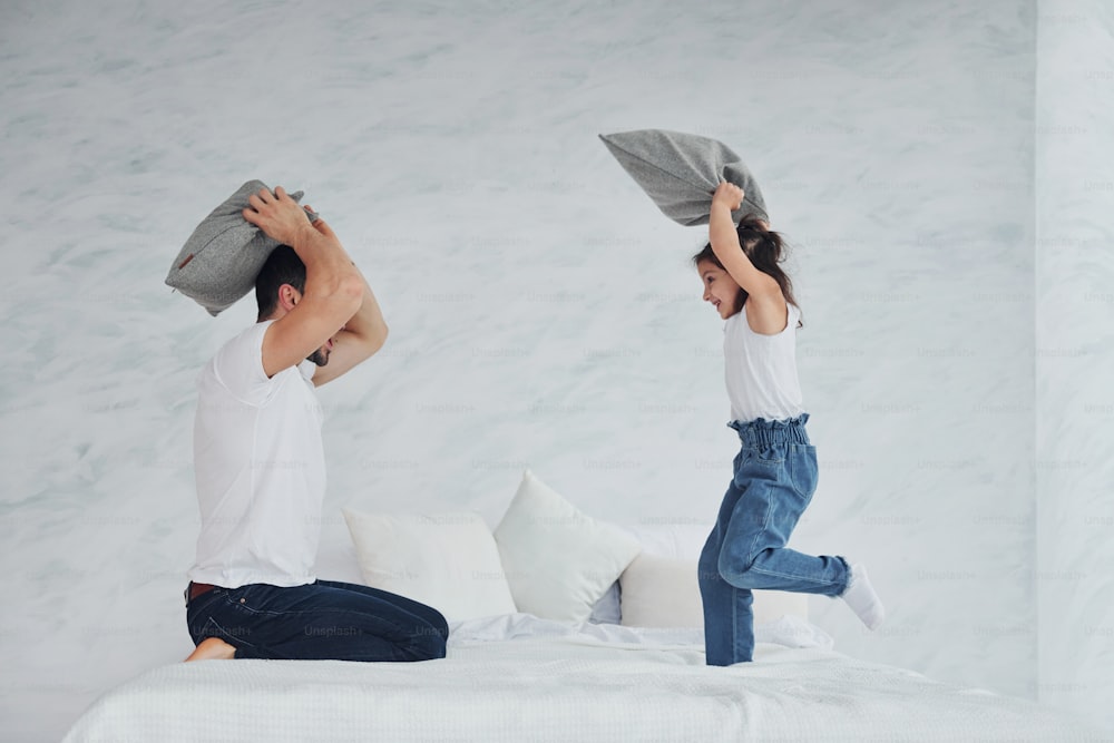 Happy father with his daughter playing pillow fight at free time at home together.