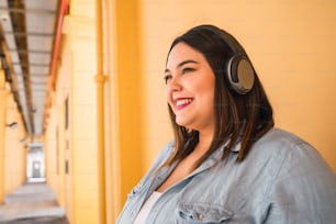 Portrait of young plus size woman listening to music with headphones outdoors. Urban concept.