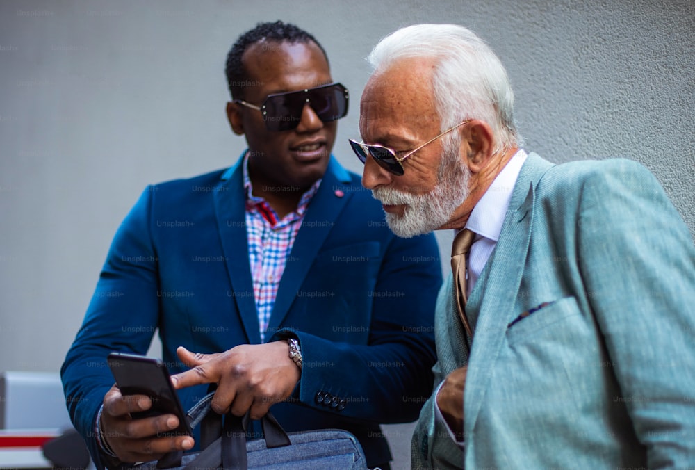 Two business men talking on the street. Man showing something to his colleague.