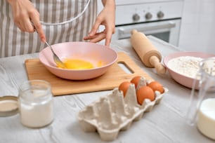 Frau schlägt Eier in einer Schüssel. Hausfrau kocht in der Küche zu Hause. Nahaufnahme
