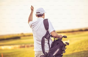 Senior golfer walking on golf court with bag.