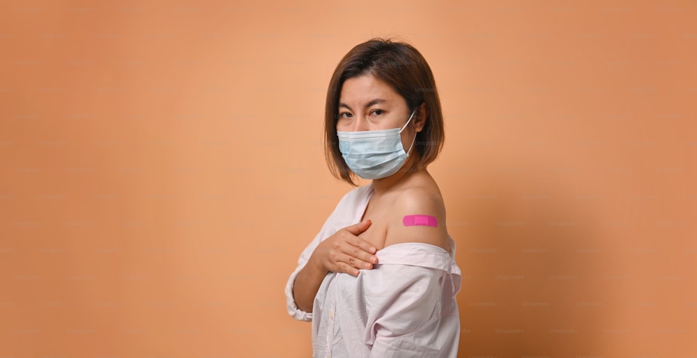 Asian woman looking at camera and showing her arm after vaccine injection.