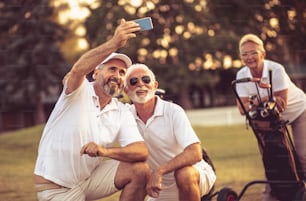 Golfistas senior usando el teléfono y tomándose un autorretrato. La atención se centra en primer plano.