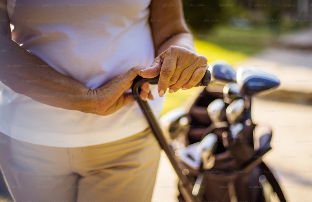 Senior woman holding bag for golf. Close up. Focus is on hands.