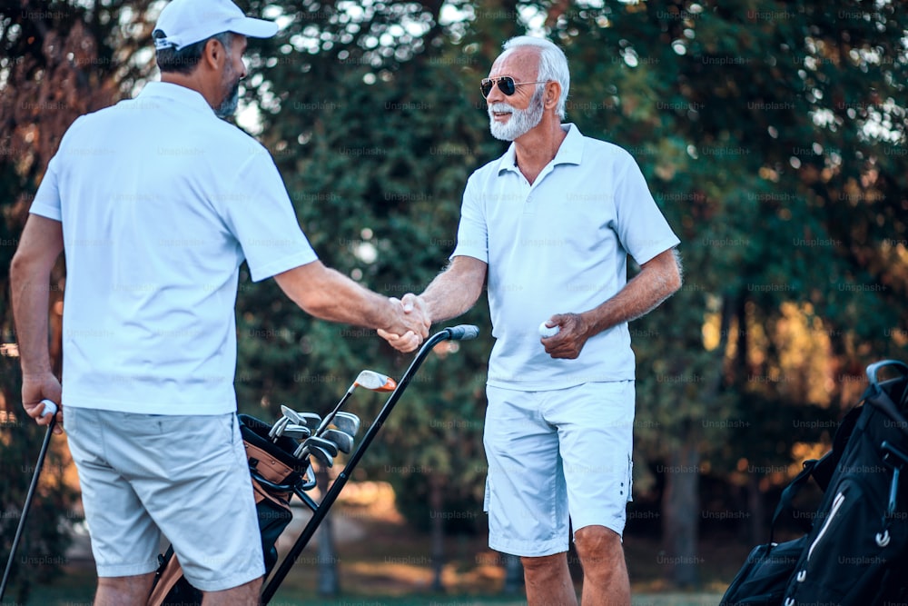 Two older men stand on a golf course and talk.