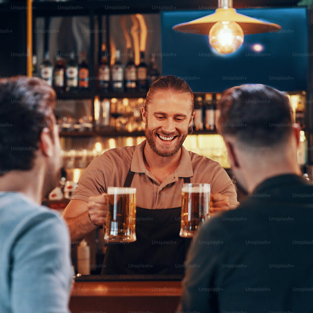 Barman joyeux servant de la bière à de jeunes hommes debout au comptoir du bar dans un pub
