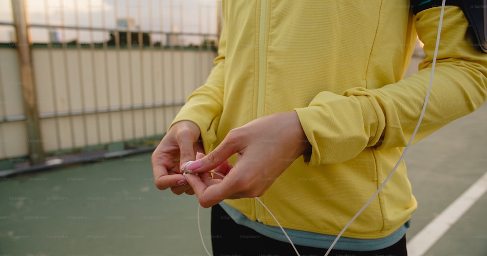 La bella giovane atleta asiatica si esercita con lo smartphone per ascoltare la musica mentre corre in ambiente urbano. Ragazza adolescente coreana che indossa abiti sportivi sul ponte pedonale al mattino presto.
