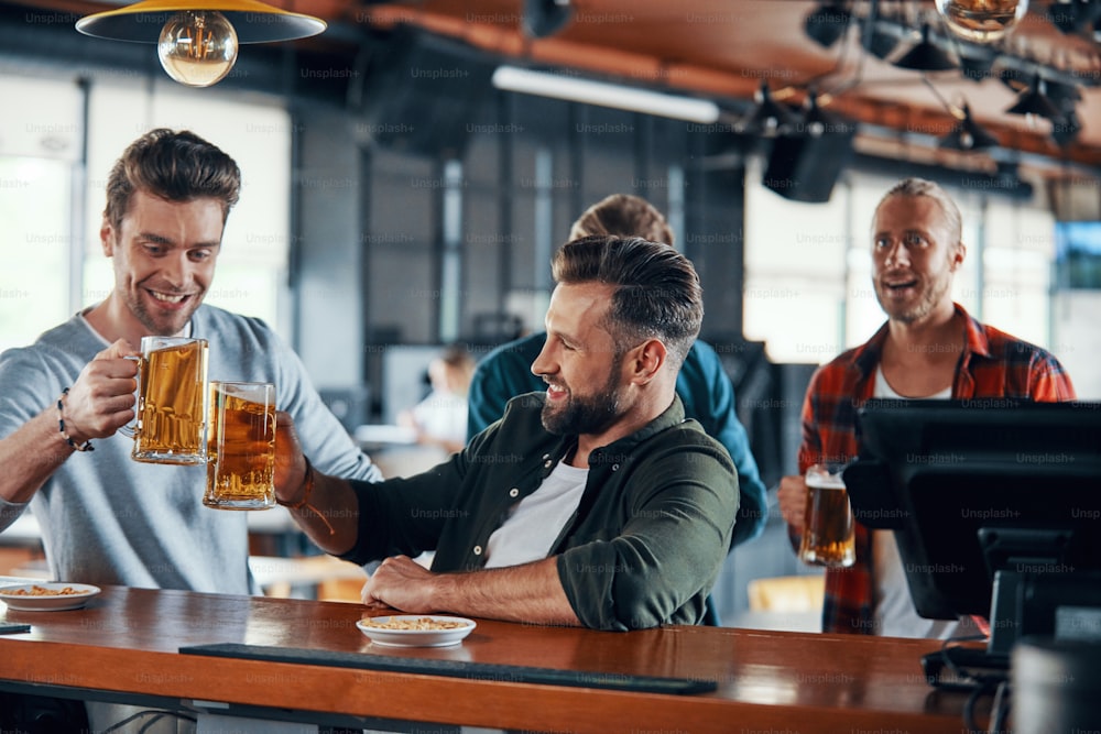 Tifare giovani uomini in abiti casual che guardano una partita sportiva e si godono una birra seduti al pub