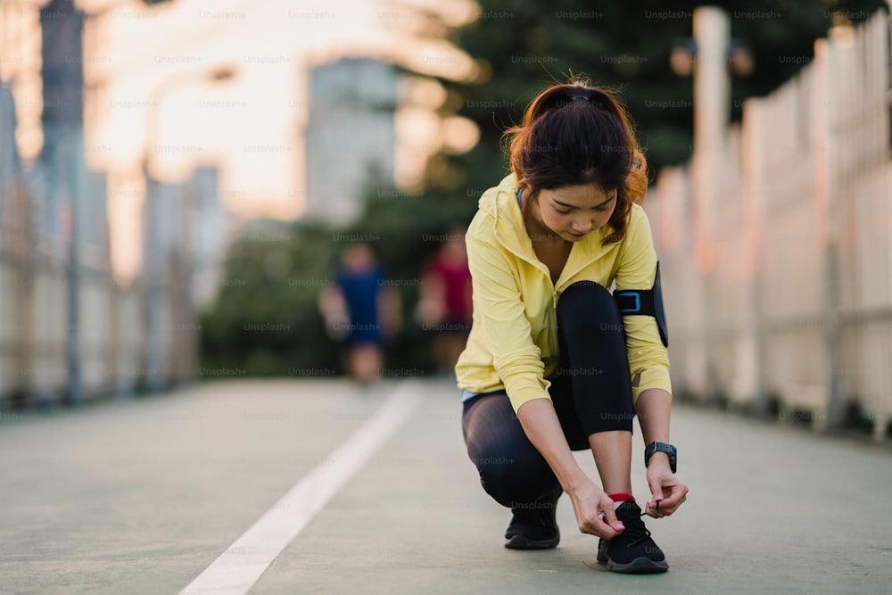 Hermosa joven atleta asiática hace ejercicios atando cordones para hacer ejercicio en un entorno urbano. Adolescente japonesa vestida con ropa deportiva en el puente de la pasarela a primera hora de la mañana. Estilo de vida activo deportivo en la ciudad.