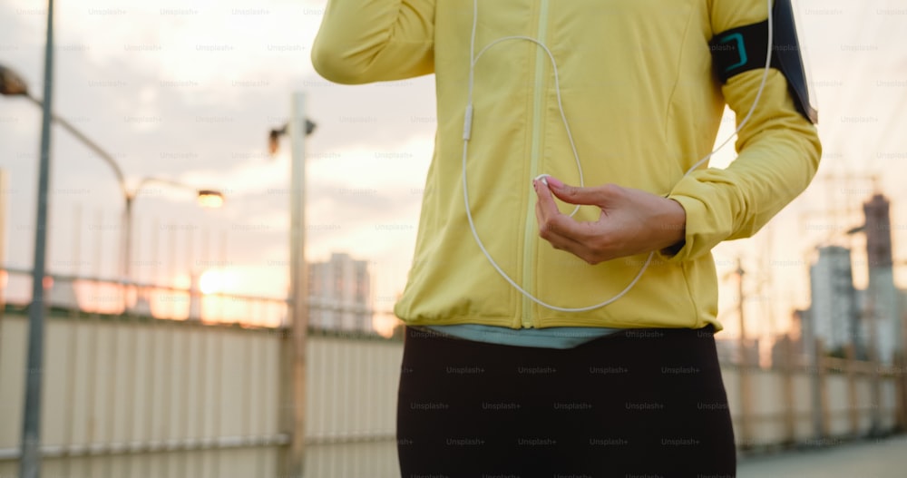 Hermosa joven atleta asiática hace ejercicio usando un teléfono inteligente para escuchar música mientras corre en un entorno urbano. Adolescente coreana vestida con ropa deportiva en el puente peatonal temprano en la mañana.