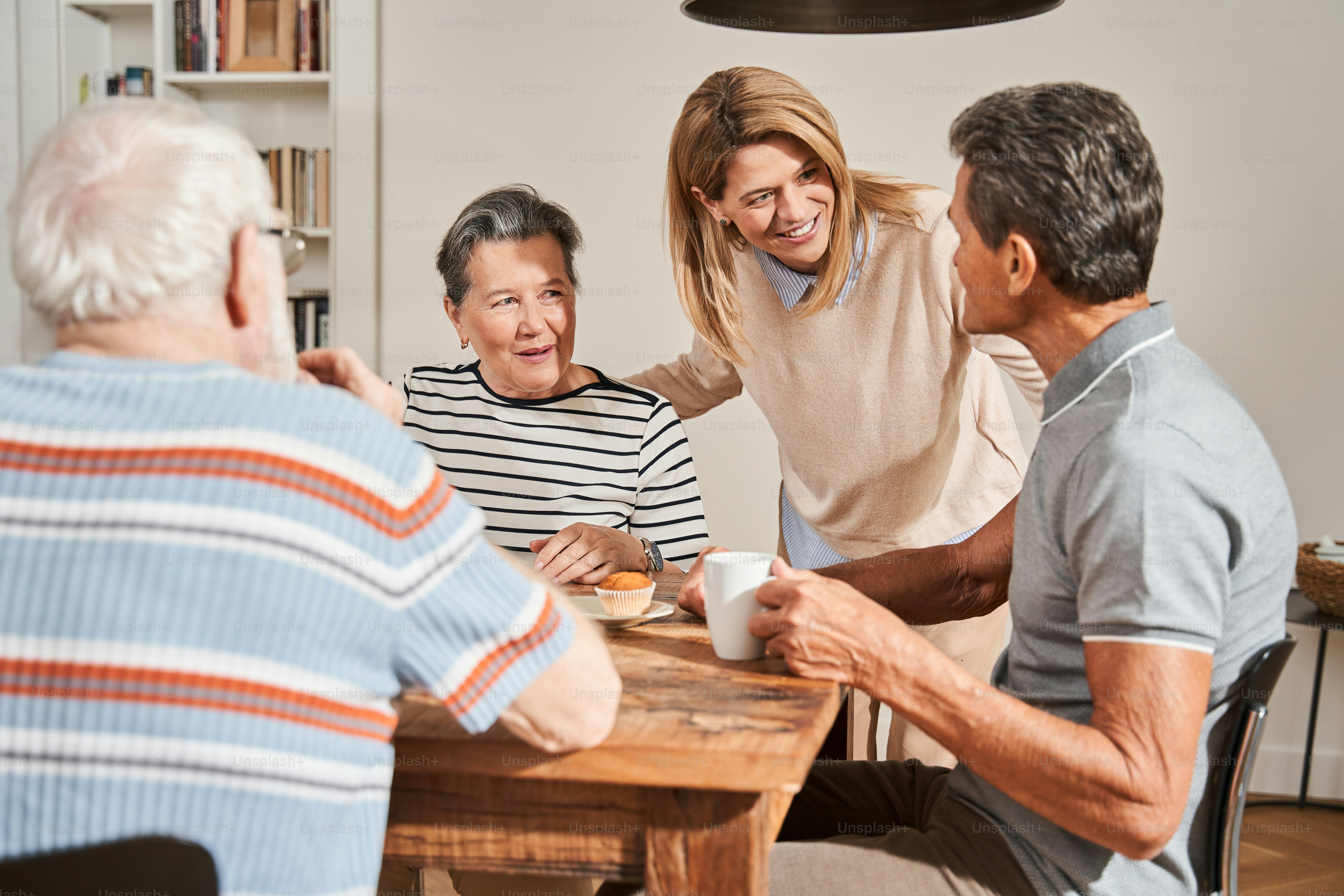 Waist up portrait view of the senior people sitting at the table and talking with friendly nurse in the retirement home. Elderly people concept