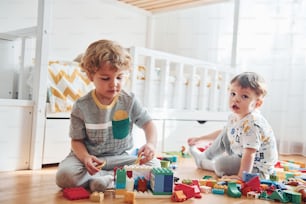 Two little boys have fun indoors in the bedroom with plastic construction set.