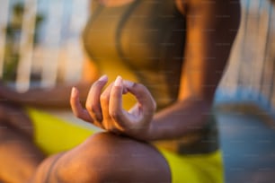 African young woman in nature sitting in yoga position on the bridge. Focus is on hand.