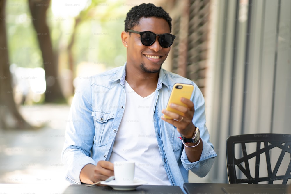 African american man using his mobile phone while sitting at a coffee shop. Urban concept.