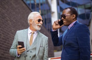 Two business men talking on the street. Using smart phones.