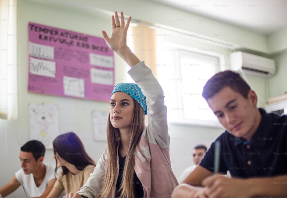 C’est une excellente élève.  Adolescentes étudiante assise dans la salle de classe et levant la main.