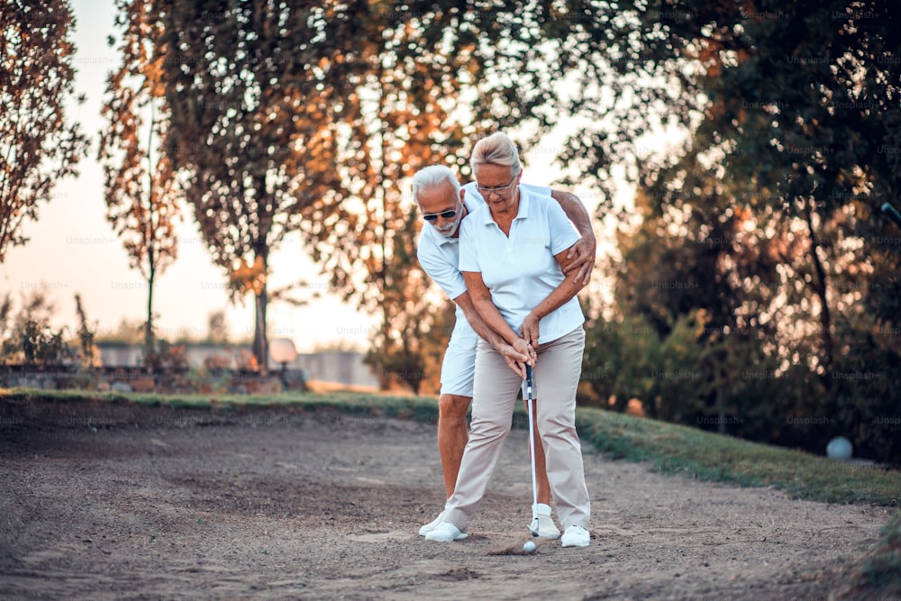 Senior couple playing golf together. Man helping woman.