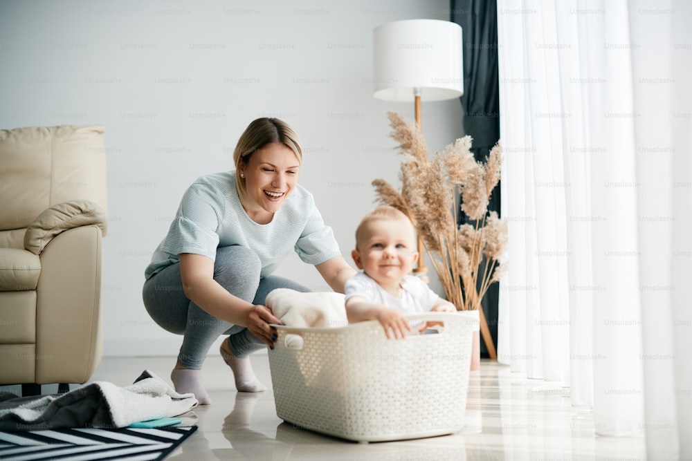 Mãe brincalhona empurrando seu bebê na cesta branca enquanto brincava com ele em casa.