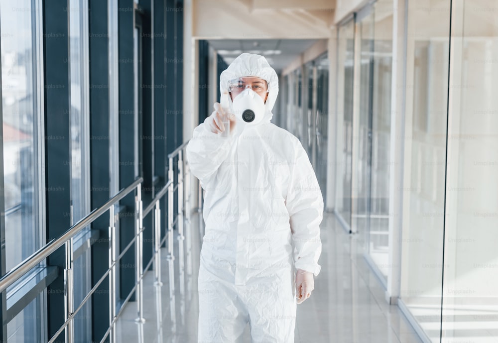 Female doctor scientist in lab coat, defensive eyewear and mask standing indoors with antibacterial spray.