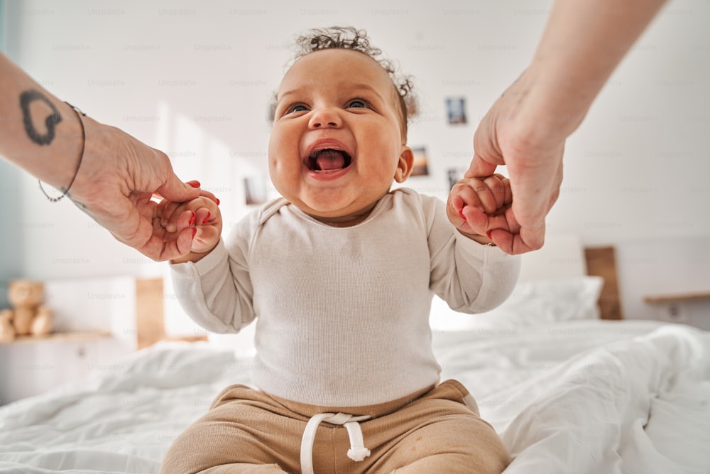 Hello. Close up view of the happy inquiring newborn boy sitting at the bed and looking at his parents attentively while spending time at the cozy bedroom