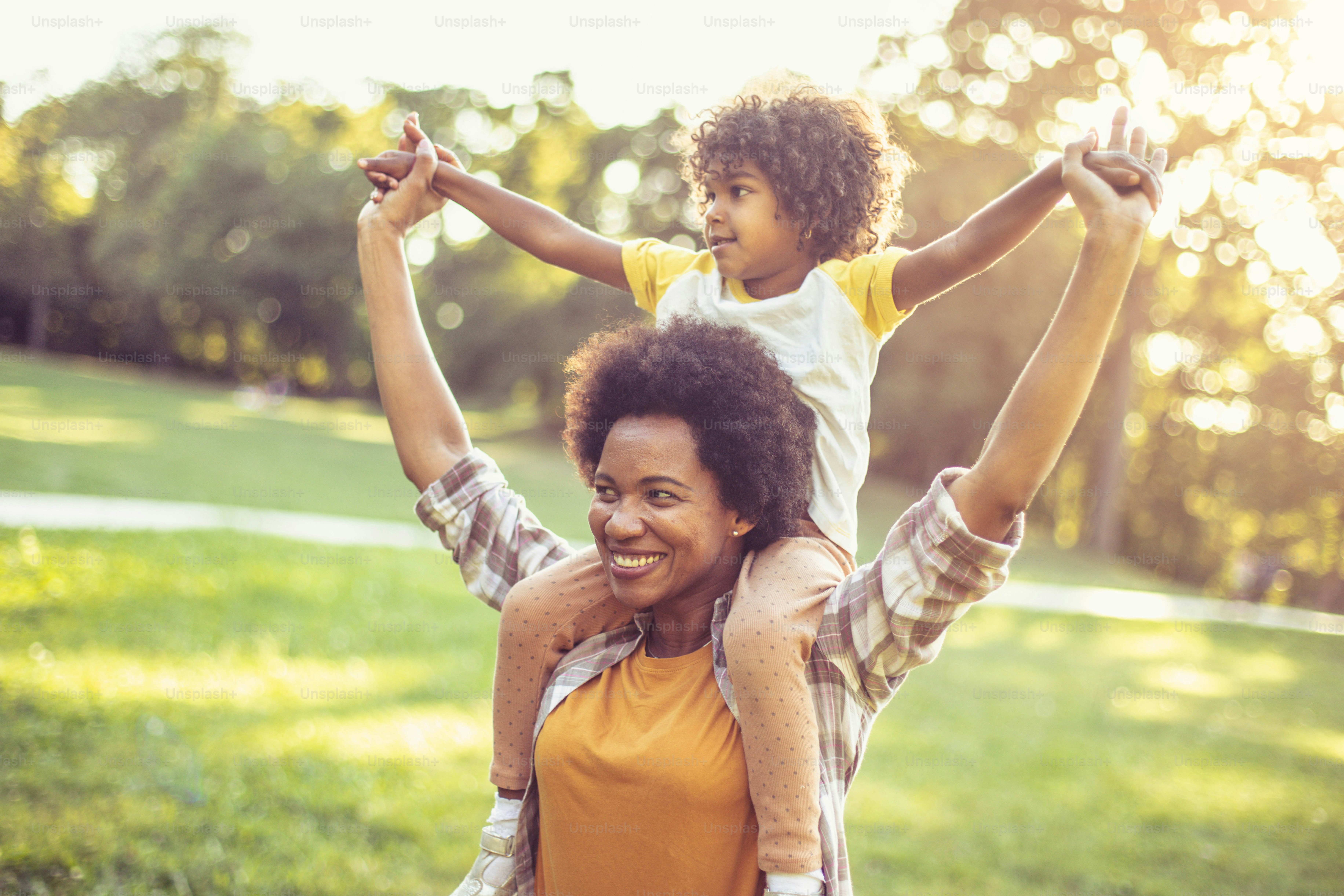 Ibu dan anak perempuan Afrika-Amerika berdiri di taman. Gadis kecil di pundak ibu.