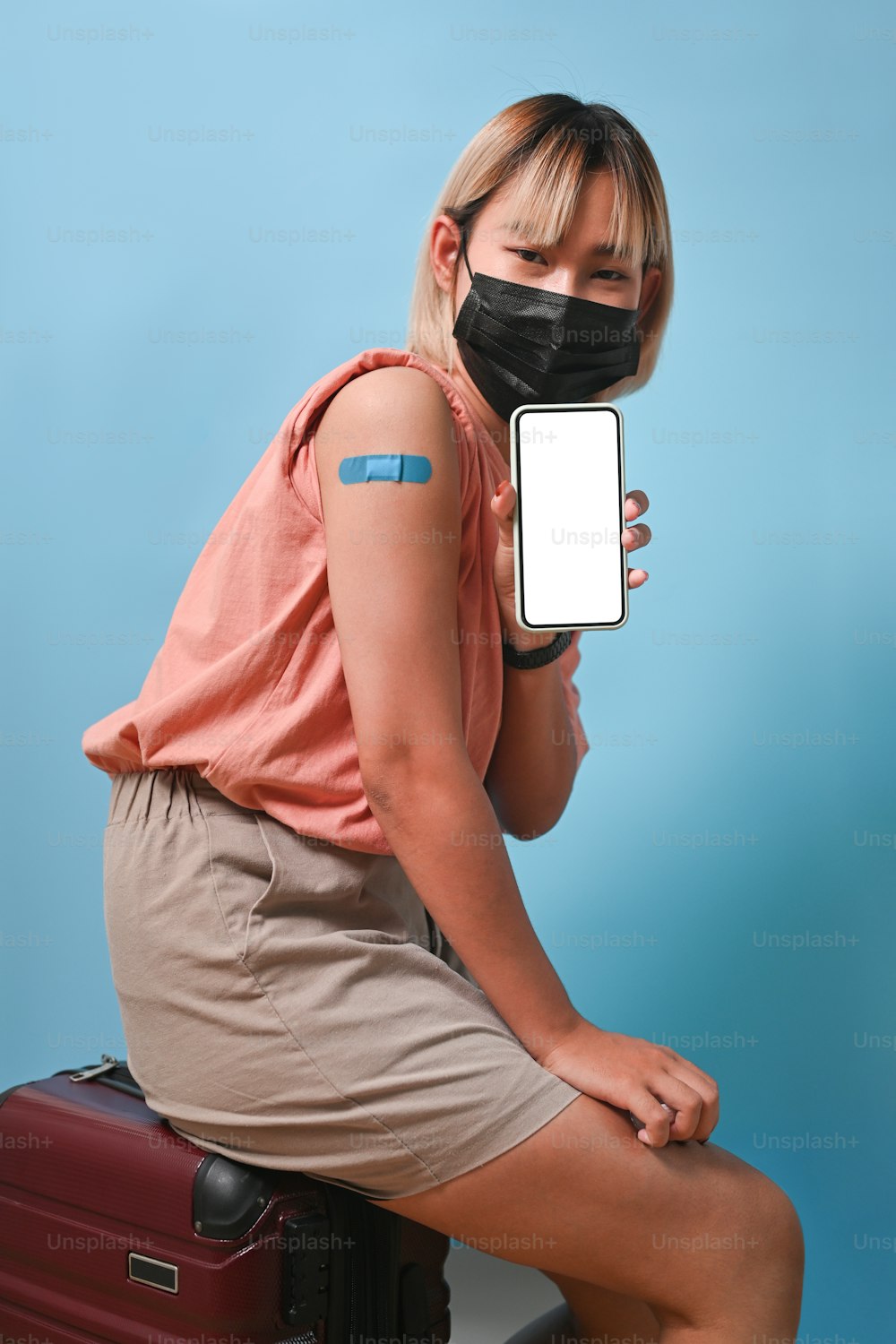 Glückliche Frau mit Gesichtsmaske, die ihr Handy hält und ihren geimpften Arm zeigt.