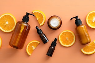 Flat lay vitamin c serum in dropper bottles, jar or cream, shower gel, shampoo with sliced orange. Top view natural fruit cosmetics.