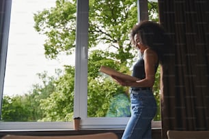 Dama atractiva sonriente con ropa informal mirando documentos en una carpeta mientras está sola. Café en la ventana