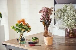 햇볕이 잘 드는 나무 테이블에 놓인 물로 채워진 투명한 유리 꽃병에 담긴 세 개의 아름다운 다색 꽃 다발