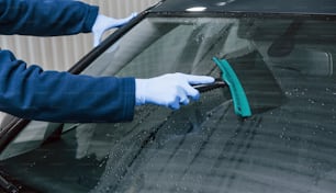 Male worker in uniform washing new modern car. Conception of service.
