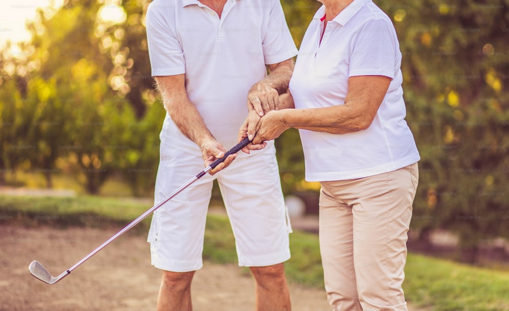 Pareja de ancianos jugando al golf juntos. Hombre ayudando a mujer en el juego.