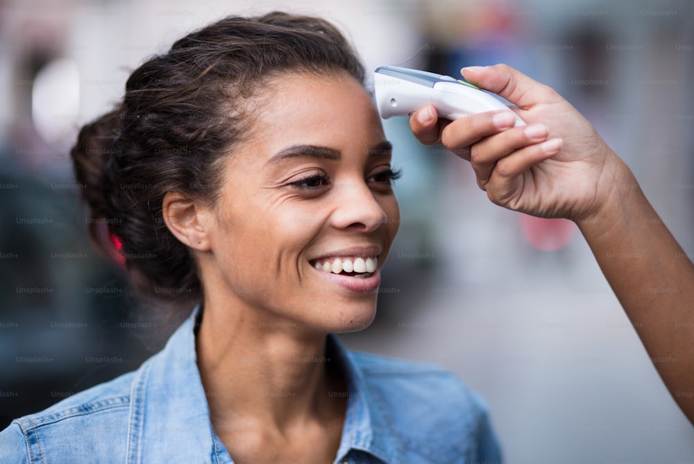 Checking body temperature for Covid 19 in a public place. Focus is on woman face.