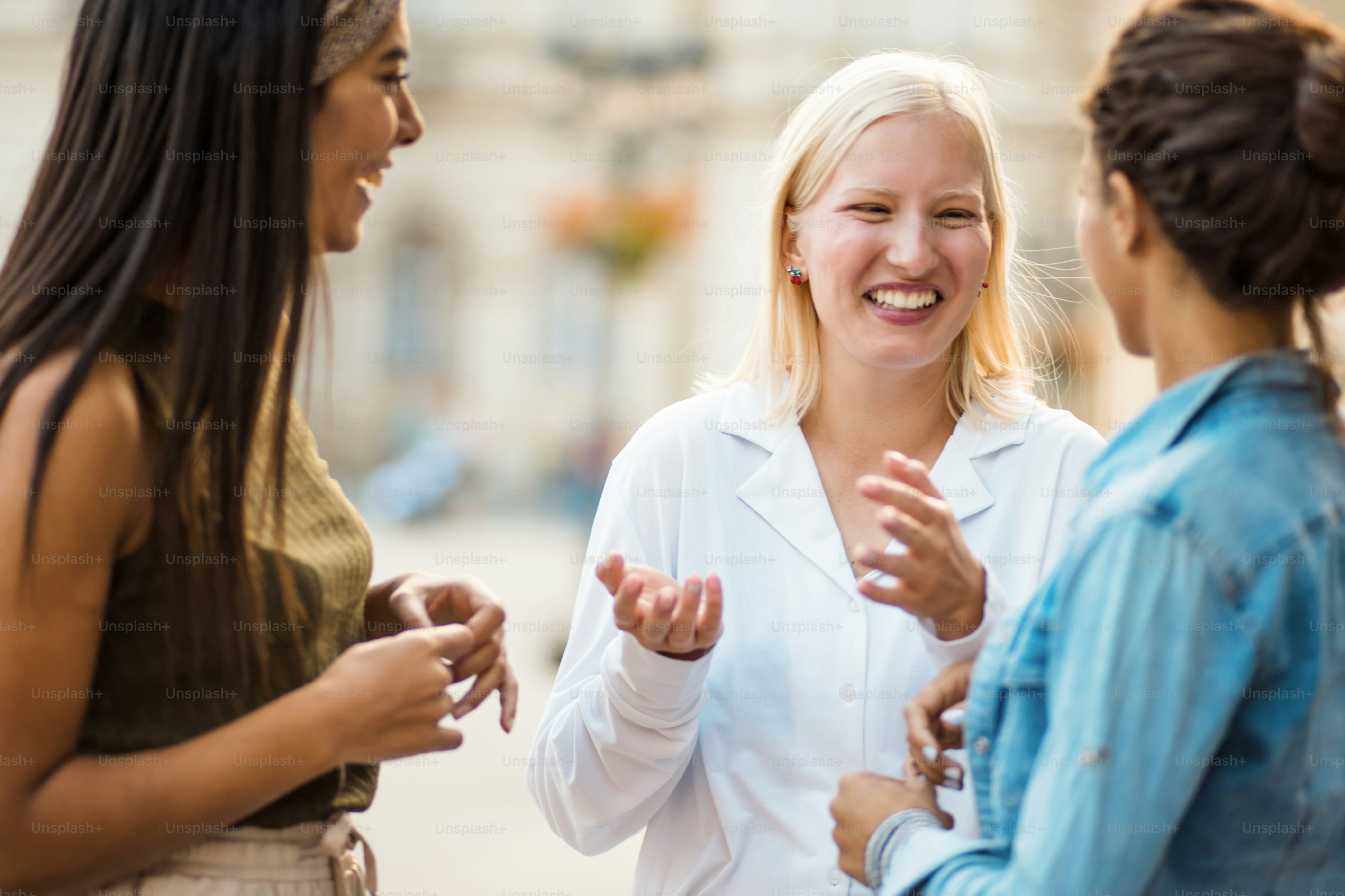 Three women standing on street and talking. Focus is on blond woman.